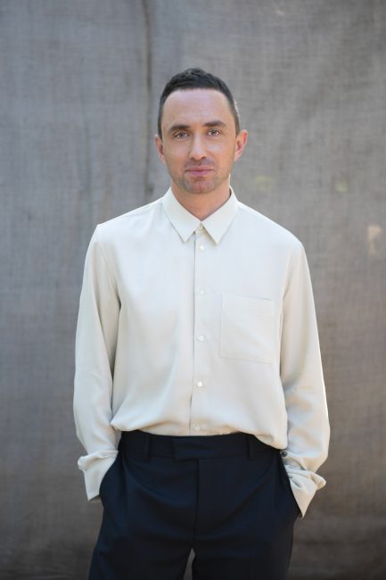 Catalin Serban im weißen Hemd, draußen vor einem grau strukturierten Hintergrund